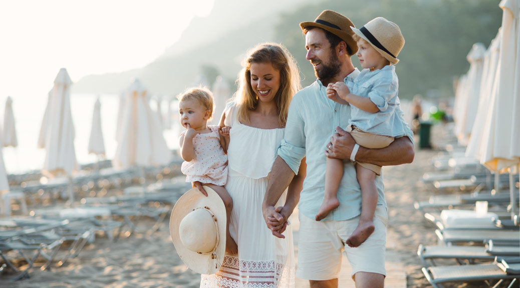 Young family with two toddler children walking on beach